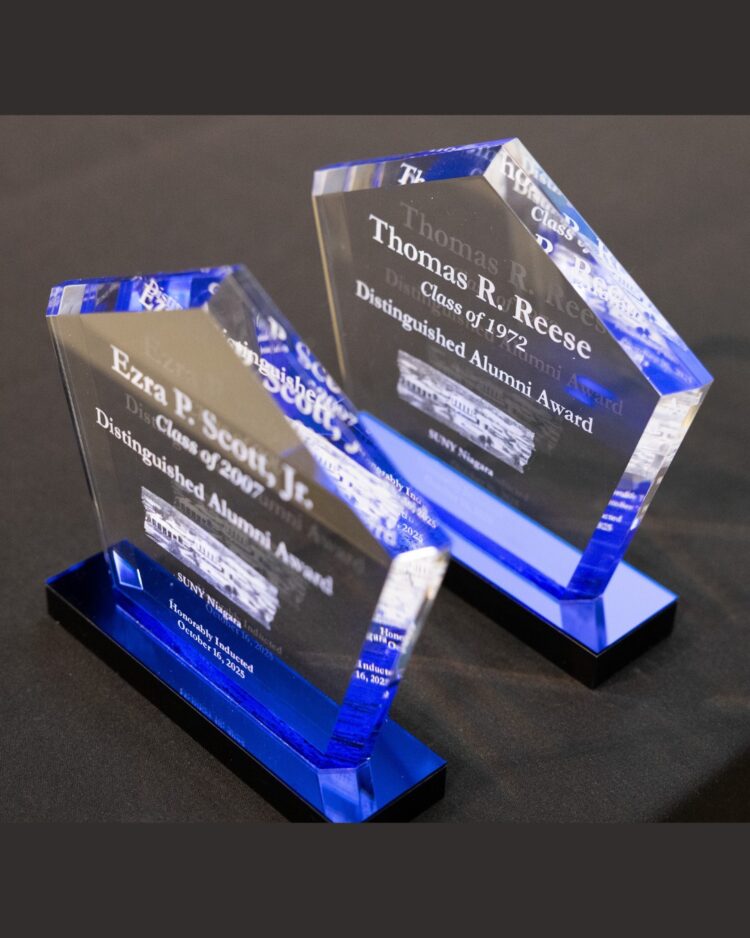 Two blue and clear glass awards engraved with the names Ezra P. Scott, Jr. and Thomas R. Reese and the words Distinguished Alumni Award stand on a black surface.