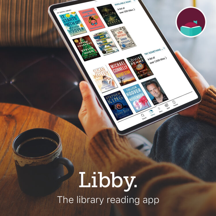 A person holds a tablet displaying the Libby app with book covers, next to a cup of coffee on a wooden table. The text reads: Libby. The library reading app. An app icon is in the top right corner.