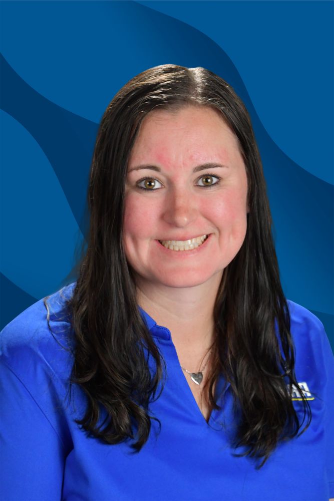 Woman with long dark hair wearing a blue collared shirt and a heart-shaped necklace, smiling in front of a blue abstract background.
