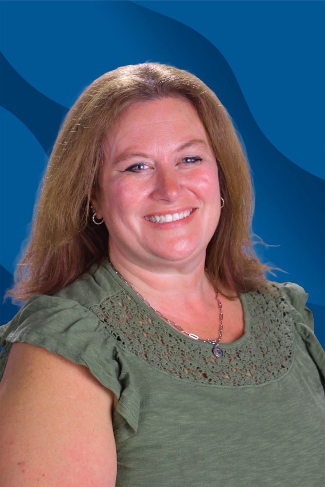 A woman with light brown hair, wearing a green top with lace details and a necklace, smiles in front of a blue wavy background.