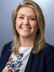 A smiling woman with shoulder-length blonde hair wearing a navy blue blazer over a floral blouse.