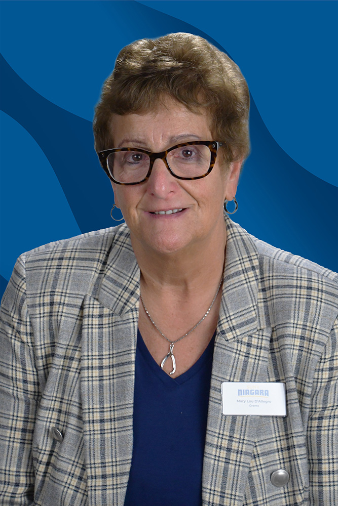 A woman wearing glasses and a plaid blazer with a Niagara name tag that reads Mary Lou DAllegro, Grants.