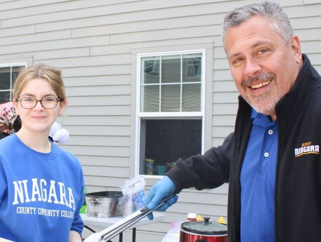 A young woman and a man in a SUNY Niagara jacket stand together at an outdoor event.